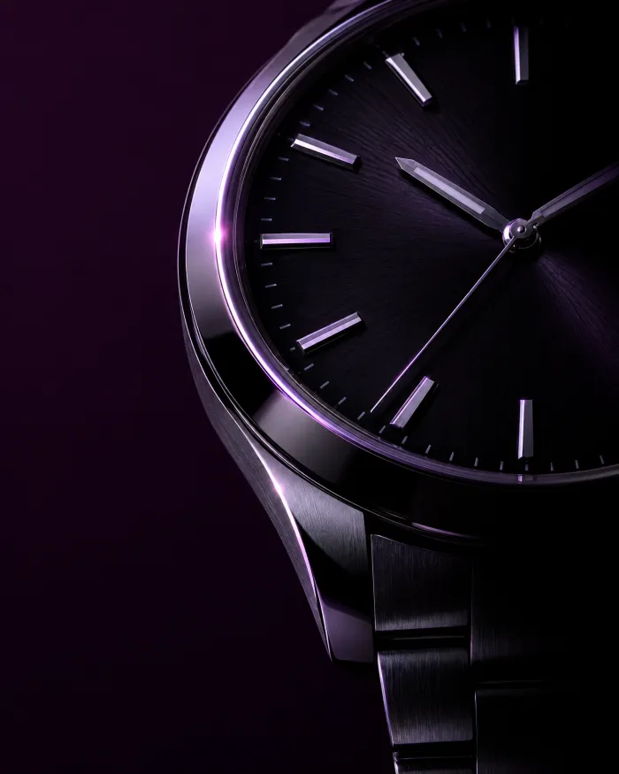 A steel wristwatch emerging from shadow under a soft violet light